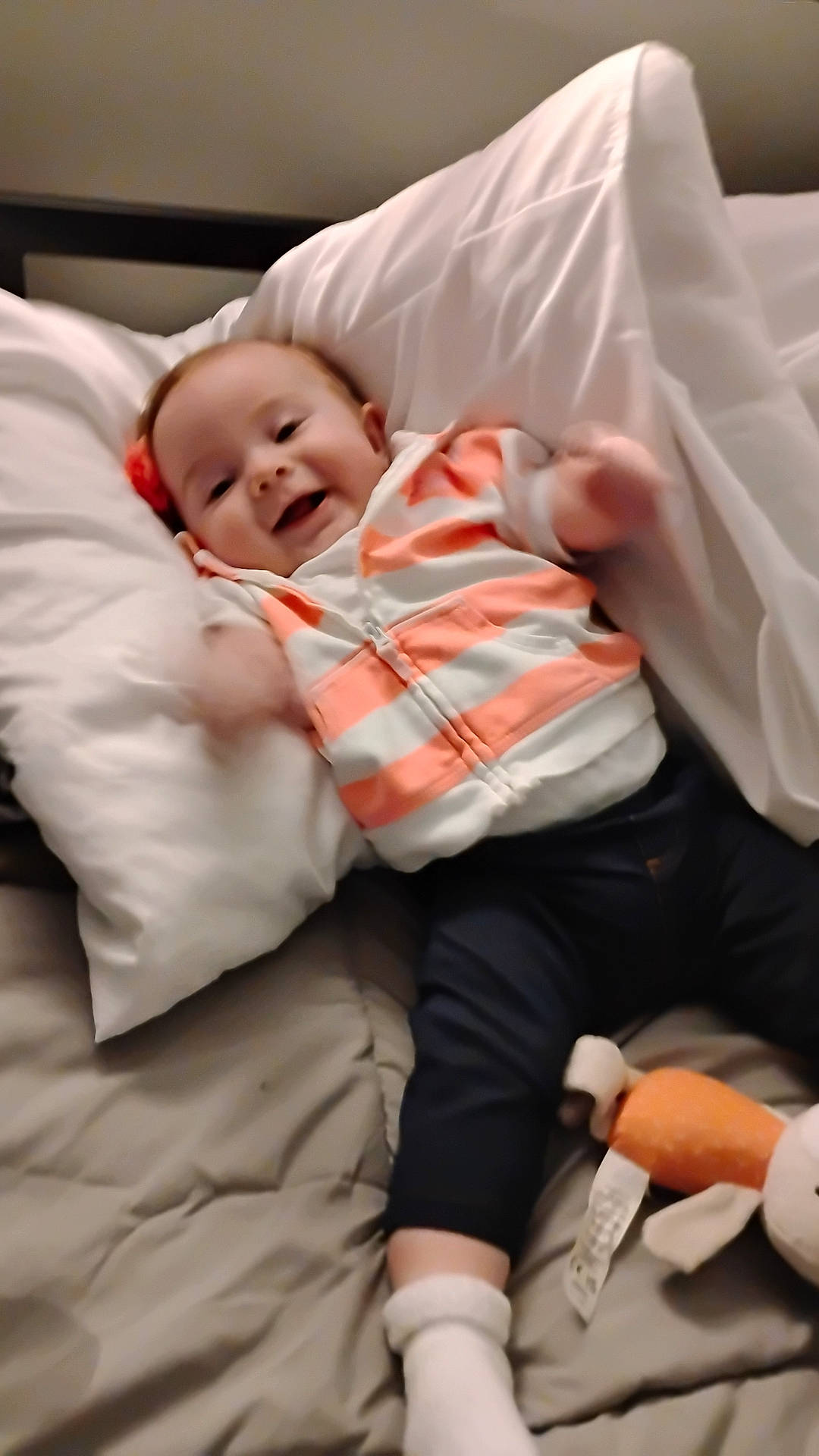 baby, bed, blanket, child, clothing, cute, happy, hoodie, indoor, infant, lying_down, motion_blur, pants, person, pillow, playful, plush_toy, smiling, socks, toy