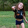 animal_shirt, backyard, black_shirt, casual_clothing, child, daylight, facial_expression, foliage, garden, girl, grass, long_hair, nature, outdoor, playful, portrait, posing, shorts, standing, trees
