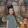 autumn, backdrop, barrels, bow, child, decorations, dress, flowers, fruit, girl, grapes, grapevines, hair, harvest, indoor, photograph, portrait, pumpkins, smiling, standing