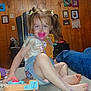 Delilah joined the competition — help win amazing prizes! child, toddler, pacifier, toy, floor, pigtails, indoor, wood_paneling, framed_photos, jeans, barefoot, playful, person, furniture, light, button, casual_clothing, smile, hair_ties, home