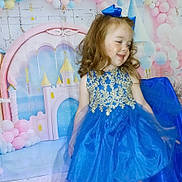 Delilah is registered to the contest to win money with this photo: child, girl, blue_dress, golden_embroidery, smiling, curly_hair, bow, party_backdrop, castle, balloons, celebration, happy, portrait, indoor, dress, tulle, costume, fashion, cute, event