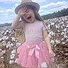blue_sky, bow, child, clouds, cotton_field, cotton_plants, daylight, farmland, fashion, girl, hat, nature, outdoor, pink_dress, playful, portrait, skirt, smiling, standing, tutu