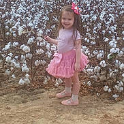 Delilah is registered to the contest to win money with this photo: agriculture, child, cotton_bolls, cotton_field, daylight, fashion, girl, hair_bow, long_hair, nature, outdoor, pink_dress, pink_skirt, plants, portrait, shoes, smiling, socks, standing, toddler