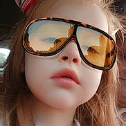 Delilah is registered to the contest to win money with this photo: child, girl, sunglasses, reflection, face, portrait, long_hair, bow, holiday, casual_clothing, white_shirt, close_up, young, fashion, indoor, cute, expressionless, headwear, accessory, person