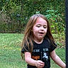 backyard, black_shirt, brown_hair, child, daylight, foliage, garden, girl, graphic_tshirt, grass, long_hair, open_mouth, outdoor, playful, portrait, smiling, standing, summer, trees, unicorn