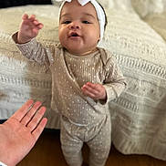 Leilani is registered to the contest to win money with this photo: baby, child, headband, bow, polka_dot, outfit, standing, hand, interaction, blanket, knitted, home, floor, curious, playful, person, skin, foot, indoor, cozy