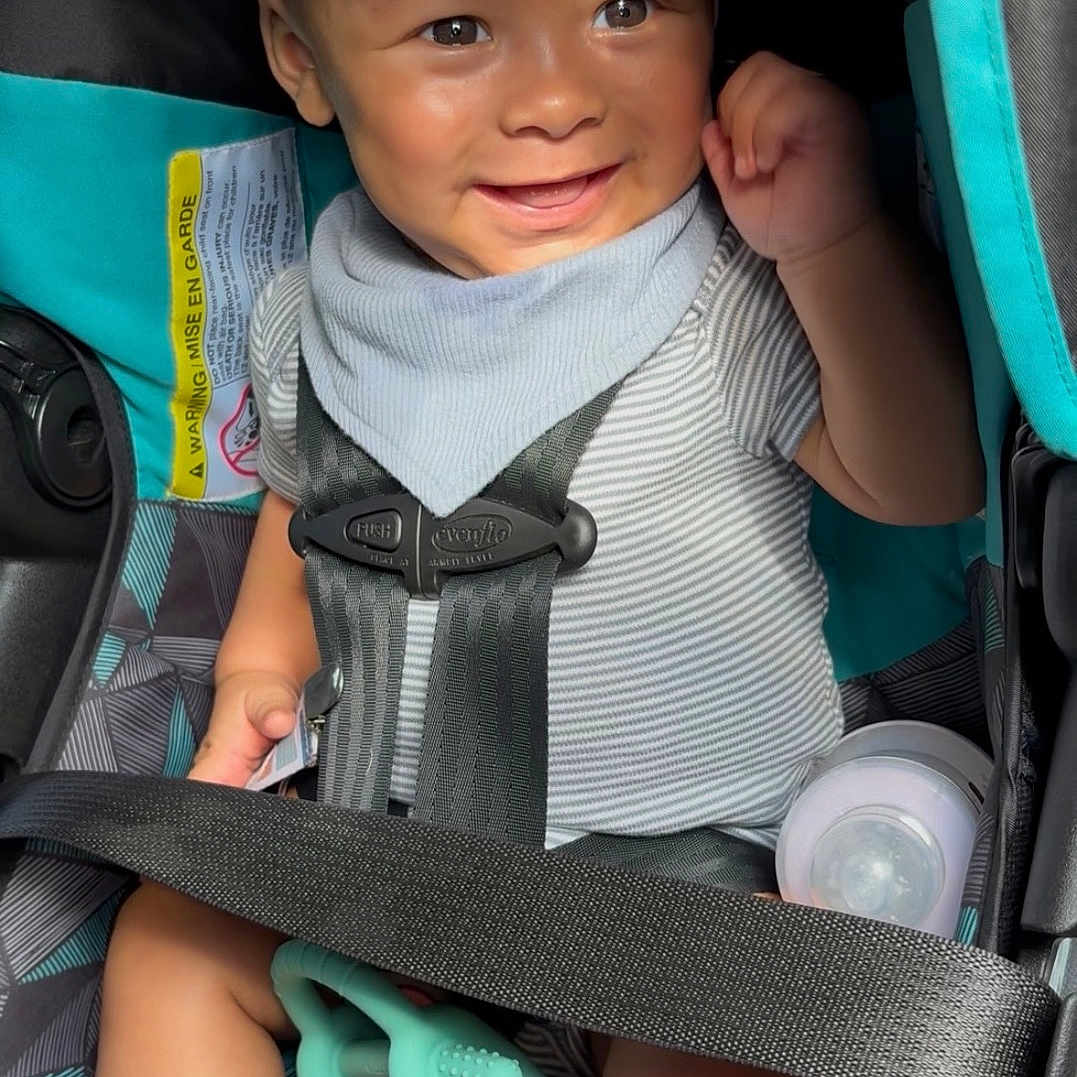John joined the competition — help win amazing prizes! baby, car_seat, smiling, toy, bottle, striped_clothing, bib, seatbelt, infant, sunlight, happy, child, sitting, hand_raised, face, cute, indoor, safety, comfort, playful