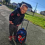 child, boy, outdoor, sunny, backpack, spiderman, jacket, shoes, smiling, pavement, grass, house, fence, blue_sky, casual_clothing, young, happy, daytime, person, toy
