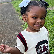 Khiari Easley is registered to the contest to win money with this photo: child, toddler, outdoor, sidewalk, grass, car, white_shirt, hair_bows, curly_hair, smiling, earrings, walking, young_child, greenery, casual_clothing, portrait, daylight, happy, person, cute