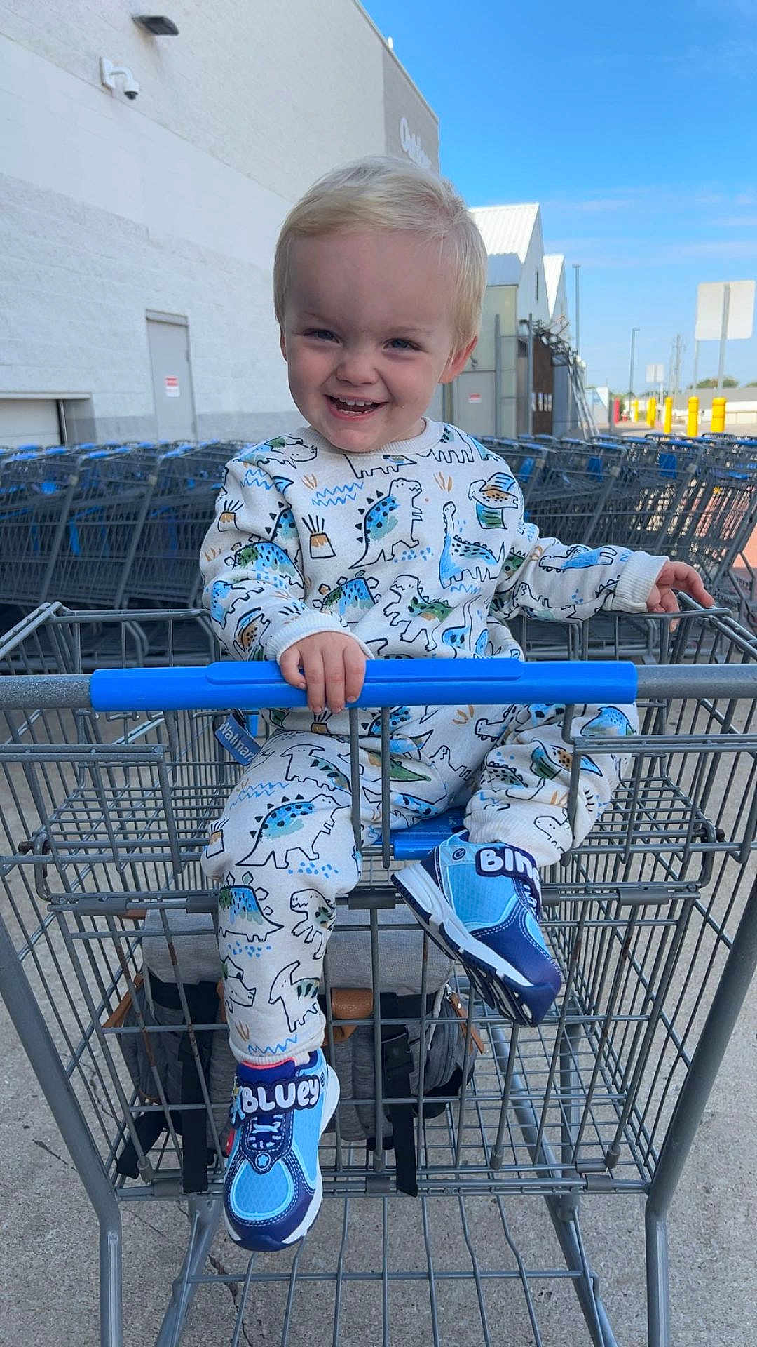 Hunter joined the competition — help win amazing prizes! toddler, child, shopping_cart, dinosaur_print, blue_shoes, outdoor, smiling, happy, clothing, footwear, concrete, metal, sky, daylight, store, retail, person, seat, grip, background