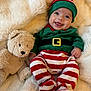baby, infant, christmas_elf_costume, striped_clothing, teddy_bear, stuffed_animal, smile, happy, cute, holiday, festive, plush, soft_texture, blanket, cozy, child, portrait, indoors, cute_outfit, hat