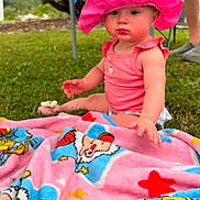 Judith joined the competition — help win amazing prizes! baby, child, pink_hat, cow_print, blanket, outdoor, grass, colorful, cartoon, clothing, sitting, person, summer, sunhat, cute, pout, greenery, legs, footwear, nature