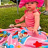 baby, child, pink_hat, cow_print, blanket, outdoor, grass, colorful, cartoon, clothing, sitting, person, summer, sunhat, cute, pout, greenery, legs, footwear, nature