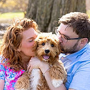 Cooper joined the competition — help win amazing prizes! dog, couple, outdoor, tree, affection, hug, kiss, happy, pet, animal, smile, glasses, woman, man, fur, sunlight, nature, portrait, love, casual_clothing