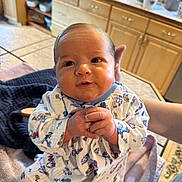 Vincent joined the competition — help win amazing prizes! baby, infant, child, onesie, clothing, hands, face, person, indoor, kitchen, cabinet, countertop, plant, window, towel, table, adult_hand, smile, cute, portrait