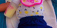 Amoura is registered to the contest to win money with this photo: baby, sleeping, bib, bottle, yellow_hat, shorts, sandals, toddler, clothing, peaceful, infant, cute, resting, child, portrait, indoors, smiling, hand_bracelet, floral_pattern, blanket