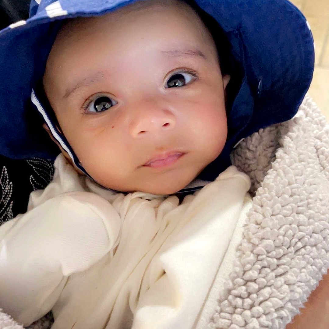 Taj is registered to the contest to win money with this photo: baby, baseballcap, blanket, bonnet, cap, clothing, coat, costume, face, hat, head, hood, jacket, knitwear, pants, person, photography, portrait, sunhat, towel