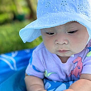 Athena is registered to the contest to win money with this photo: baby, child, hat, white_hat, purple_shirt, colorful_prints, hands, blue_blanket, outdoor, green_background, infant, cute, portrait, close_up, skin, person, sunhat, summer, nature, baby_fashion