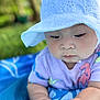 baby, child, hat, white_hat, purple_shirt, colorful_prints, hands, blue_blanket, outdoor, green_background, infant, cute, portrait, close_up, skin, person, sunhat, summer, nature, baby_fashion