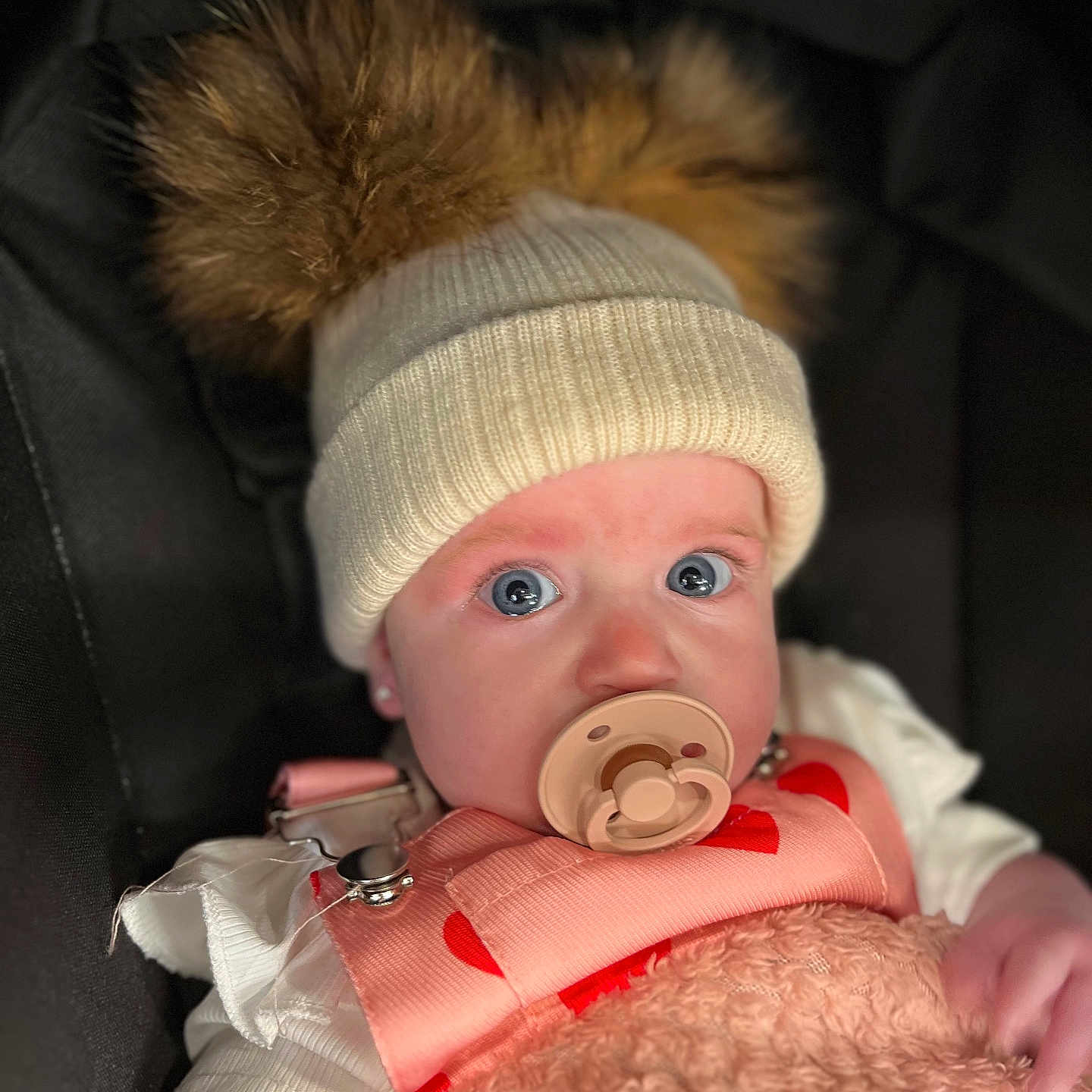 Willow-Sophie is registered to the contest to win money with this photo: baby, blanket, blue_eyes, child, closeup, clothing, cozy, cute, face, hat, indoor, infant, pacifier, pink, pom_poms, portrait, sitting, soft_texture, warm, white