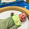 Mateo joined the competition — help win amazing prizes! baby, infant, smiling, green_onesie, bib, play_area, padded, circular, blue_carpet, toy, child, happy, indoors, floor, cute, face, skin, cheeks, lying_down, early_childhood