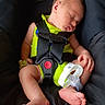 newborn, baby, sleeping, car_seat, safety_harness, bright_clothing, hospital_band, infant, foot, hand, face, resting, child, transportation, seat, black_background, cute, peaceful, tiny_toes, portrait