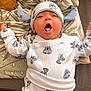 baby, blanket, cartoon_print, child, clothing, cozy, cushion, cute, expression, hat, headwear, indoors, infant, lying_down, onesie, pattern, person, sleepy, soft_fabric, yawning