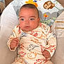 adorable, animal_print, baby, baby_chair, child, clothing, colorful, cute, dinosaur_print, expression, face, furniture, indoor, infant, pajamas, person, seated, soft_lighting, wood_floor, young