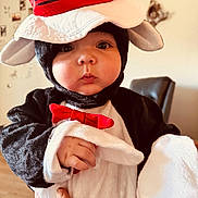 Weston is registered to the contest to win money with this photo: baby, child, costume, penguin, hat, red_bow_tie, plush, cute, indoor, person, face, hand, expression, black, white, soft, clothing, portrait, looking, adorable