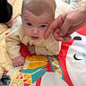 adult_hand, baby, bedroom, close_up, colorful_mat, cute, expressive, eyes, face, hand, indoor, infant, parent, patterned_blanket, photography, playing, portrait, skin, sweater, tummy_time