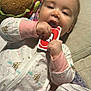 baby, child, pajamas, plush_toy, toy, uno_card, hand, face, couch, blanket, paper, indoor, clothing, infant, playing, lying_down, cute, chewing, soft_toy, relaxed