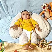 Krivam Patel is registered to the contest to win money with this photo: baby, child, yellow_clothing, pillow, blue_backdrop, toys, stuffed_tiger, giraffe_toy, broccoli, food_bowl, smiling, happy, indoor, playful, decorations, heart_sticker, moon_sticker, infant, cute, cozy