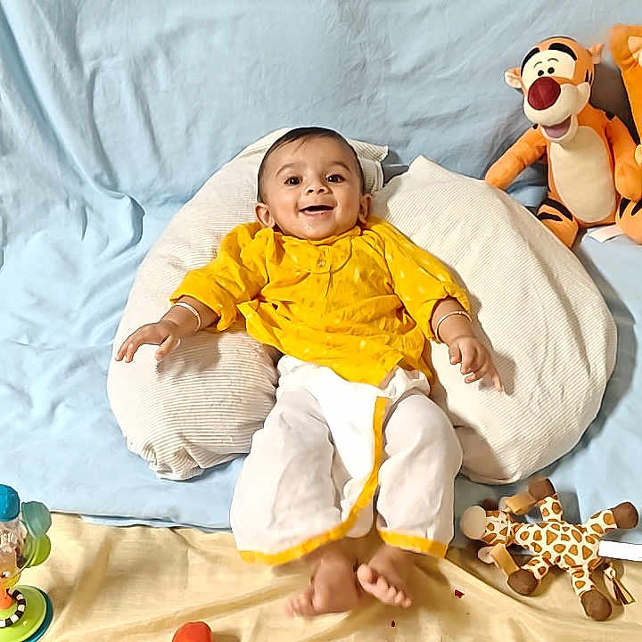 Krivam Patel is registered to the contest to win money with this photo: baby, child, yellow_clothing, pillow, blue_backdrop, toys, stuffed_tiger, giraffe_toy, broccoli, food_bowl, smiling, happy, indoor, playful, decorations, heart_sticker, moon_sticker, infant, cute, cozy