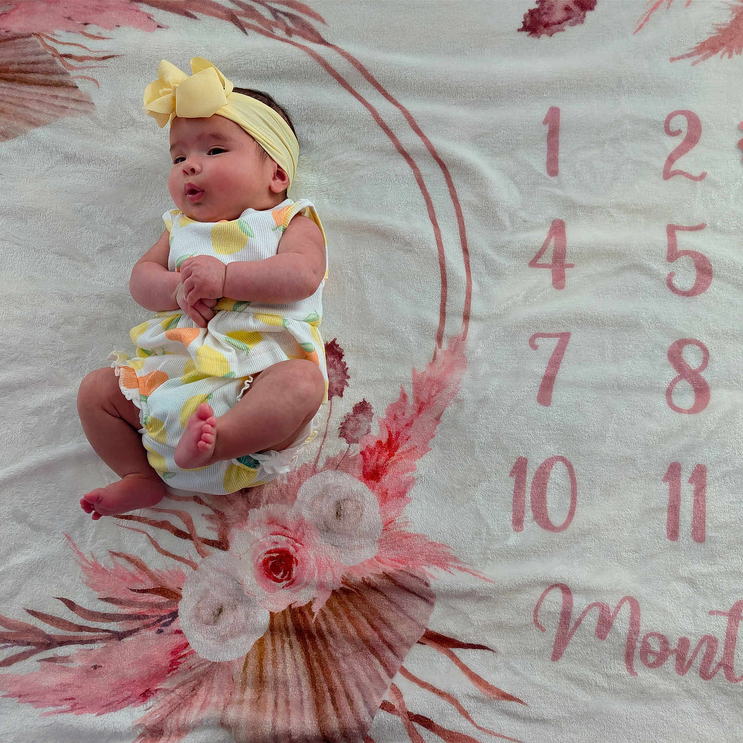Kaelynn is registered to the contest to win money with this photo: baby, infant, headband, yellow_bow, colorful_outfit, floral_blanket, numbers, months, milestone, cute, lying_down, pink, white, skin, child, portrait, celebration, soft_texture, clothing, expression