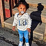 toddler, child, pacifier, curly_hair, white_sweatshirt, blue_jeans, white_sneakers, standing, outdoor, sunny_day, shadow, wooden_steps, clothing, person, young_child, cute, casual_wear, daylight, portrait, baby