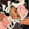 baby, child, cow_costume, hood, pink, black_and_white, plush, animal_print, leopard_print, zebra_toy, indoor, person, cute, costume, face, smile, hand, cozy, carpet, floor