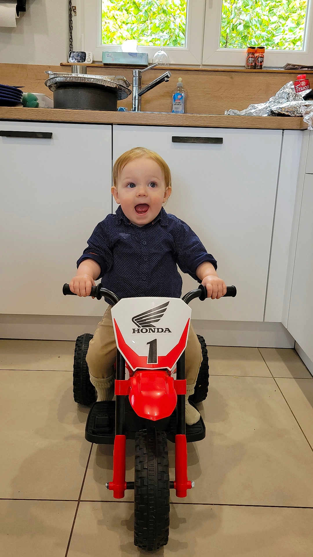 Gabriel a rejoint le concours — aidez-le/la à gagner de superbes lots ! toddler, child, toy, motorbike, indoor, kitchen, floor, happy, excited, vehicle, small, person, playing, clothing, pants, shirt, footwear, window, cabinet, handlebars