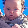 baby, infant, child, face, eyes, blue_sky, outdoor, portrait, hand, hair, sweater, clothing, person, cheeks, skin, gaze, sunlight, holding, curly_hair, expression