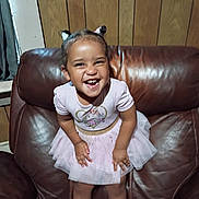 Evelyn joined the competition — help win amazing prizes! child, toddler, smiling, happy, dress, unicorn, pink, hair_buns, leather_chair, armchair, wood_paneling, indoor, cute, person, fun, joy, small_child, portrait, clothing, furniture