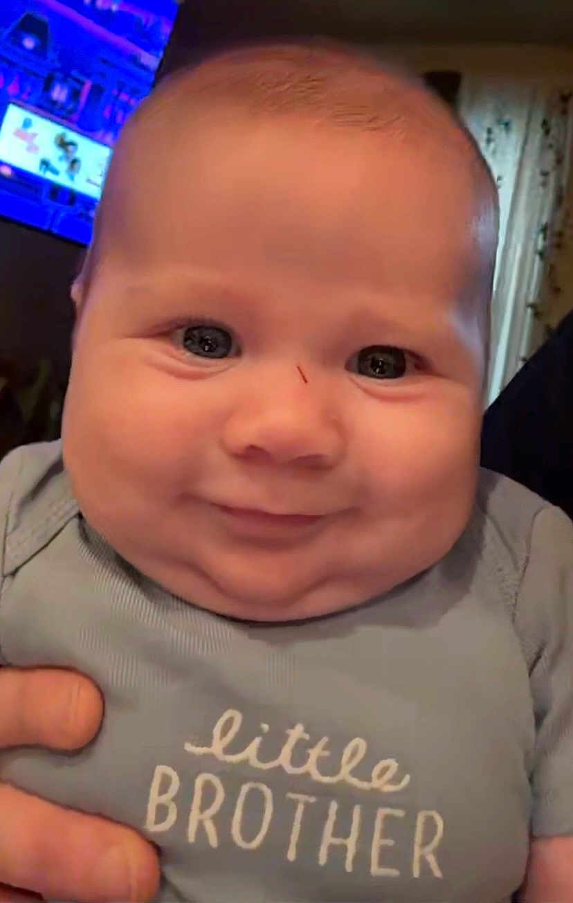 Jett is registered to the contest to win money with this photo: baby, child, smiling, face, onesie, clothing, hand, indoor, portrait, cute, chubby_cheeks, little_brother, infant, human, person, expression, holding, background, screen, home