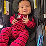 Dario joined the competition — help win amazing prizes! baby, child, infant, smiling, car_seat, harness, red_outfit, striped_clothing, portrait, indoors, vehicle, sitting, happy, face, hands, black_hair, safety_labels, automotive, cozy, photography