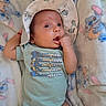 Dario is registered to the contest to win money with this photo: baby, infant, child, portrait, lying_down, blanket, hat, onesie, clothing, face, eyes, smiling, hand, fist, indoors, bed, textile, patterned_blanket, champion_shirt, photography