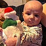 Emberly is registered to the contest to win money with this photo: baby, child, indoor, plush_toy, santa_doll, onesie, person, face, holding, furniture, door, expression, curious, cozy, patterned_clothing, infant, closeup, warm_lighting, caucasian_baby, portrait