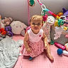 baby, child, pink_dress, playpen, plush_toys, stuffed_animals, toy_mobile, pink_mat, smiling, indoor, cute, infant, floor_mat, colorful, toddler, soft_toys, play_area, happy, girl, young_child