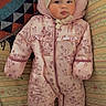 Eliana is registered to the contest to win money with this photo: baby, infant, snowsuit, pink_clothing, hat, bear_ears, couch, blanket, patterned_fabric, floral_pattern, face, child, portrait, cozy, warm_clothing, indoor, cute, lying_down, winter_wear, apparel