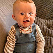 Elyano a rejoint le concours — aidez-le/la à gagner de superbes lots ! baby, infant, child, smiling, portrait, sitting, striped_shirt, knit_overall, amber_necklace, couch, cushion, knit_blanket, indoor, closeup, blue_eyes, chubby_cheeks, hand, hair, adorable, warm_lighting