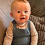 baby, infant, child, smiling, portrait, sitting, striped_shirt, knit_overall, amber_necklace, couch, cushion, knit_blanket, indoor, closeup, blue_eyes, chubby_cheeks, hand, hair, adorable, warm_lighting