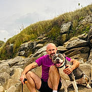 Tairo a rejoint le concours — aidez-le/la à gagner de superbes lots ! casual_clothing, companion, daylight, dog, friendship, grass, happy, hill, leash, man, nature, outdoor, pet, portrait, rock, shorts, sitting, smile, sneakers, tattoo