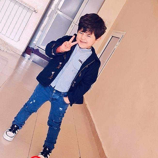 Rayane a rejoint le concours — aidez-le/la à gagner de superbes lots ! child, boy, peace_sign, smiling, casual_clothing, jacket, ripped_jeans, sneakers, indoor, hallway, tile_floor, door, wall, radiator, decorative_wall_hangings, heart_emoji, pose, young, person, playful