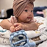 baby, infant, turban, hat, cushion, toy, teething_toy, hands, face, cheeks, curious, indoor, closeup, portrait, soft_focus, plush, clothing, resting, child, cute